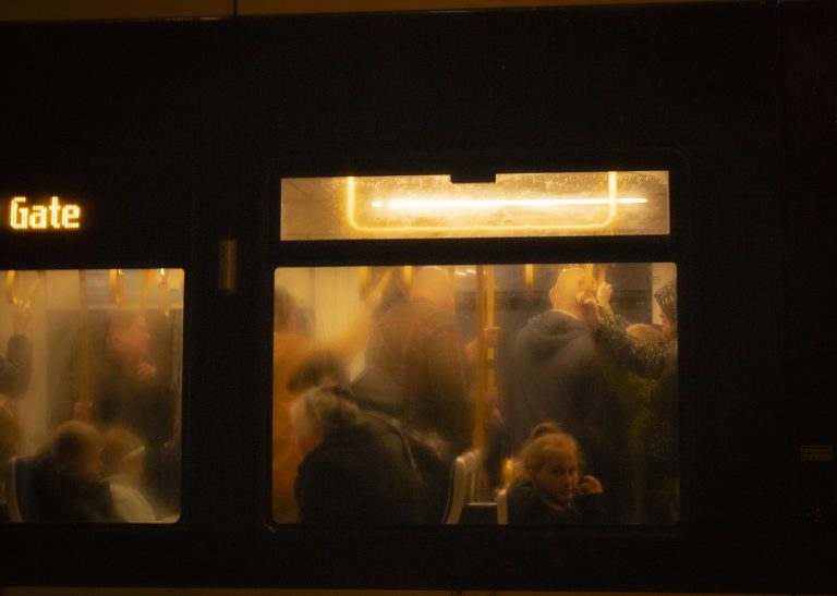A photograph taken by Sophie Allaker, capturing the window of a tram and the people inside.
