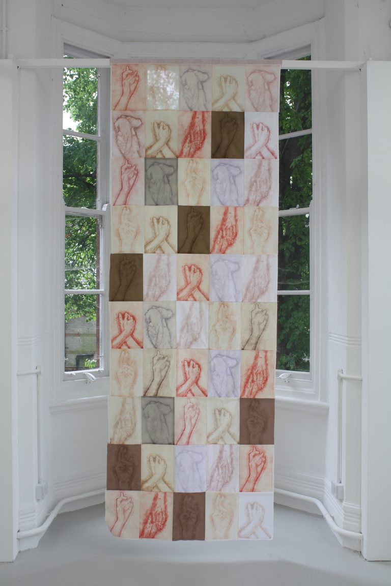 Large hanging textile work displaying repeated imagery of touching hands and Christian symbolism.