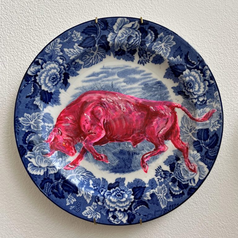 Fine Art work by Eve Harriss showing a bright pink bull painted onto a blue and white ceramic plate. the colours are very bright and playful. The piece is hung on a wall using a plate hanger.