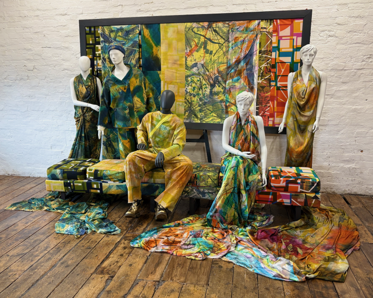 Textile designs by Annie Gough, 5 mannequins in brightly printed textiles and bench with a corresponding piece of artwork behind them.