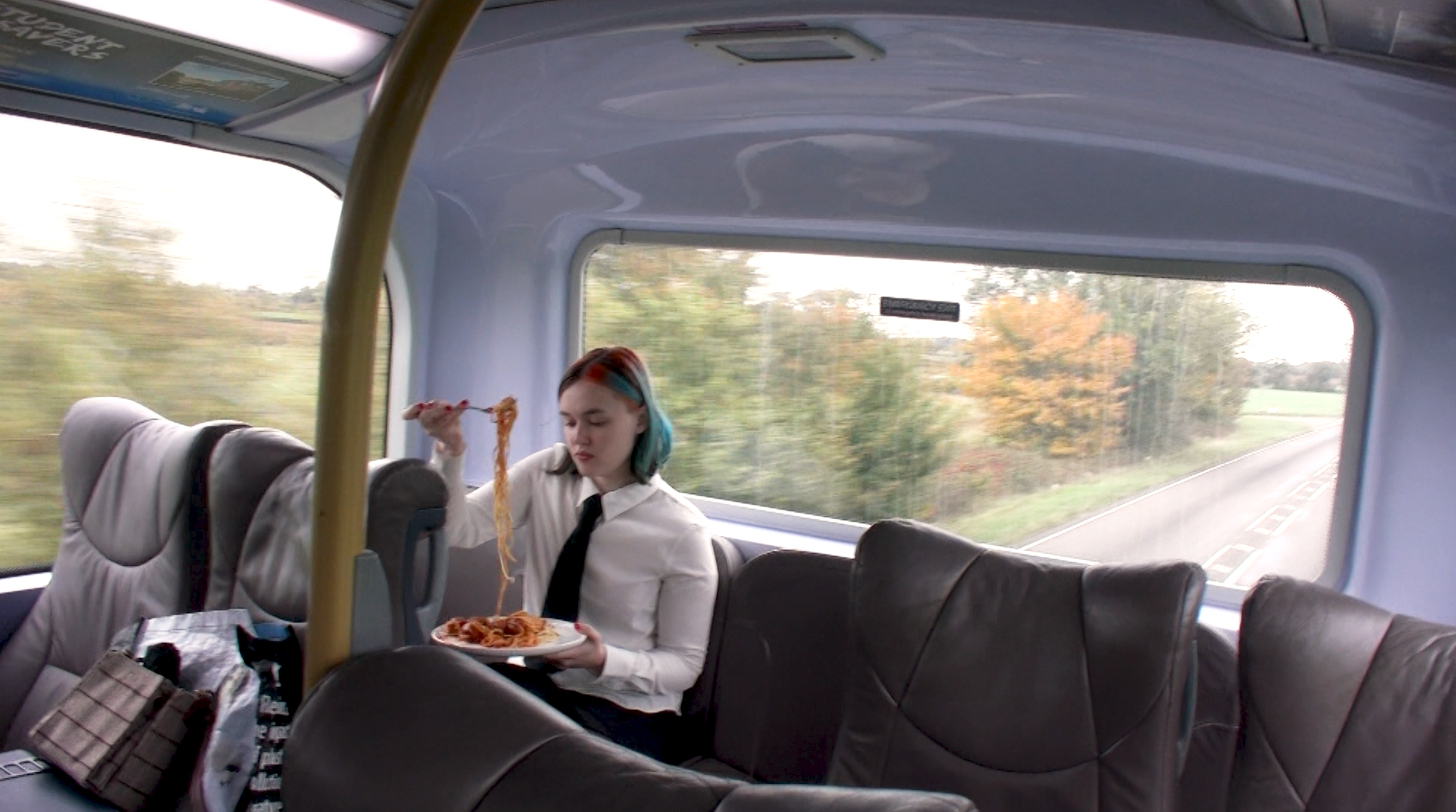 Fine Art work by Amy White documenting an eating performance that challenges fast food. It depicts two performers eating spaghetti and meatballs, and a roast chicken dinner on a bus.
