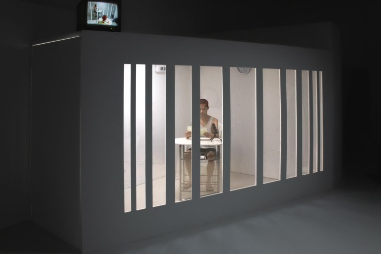 Fine Art durational performance by Marco Yuen showing the performer reading books behind mirrored windows of the constructed room, with a visible CRT on top of the room.