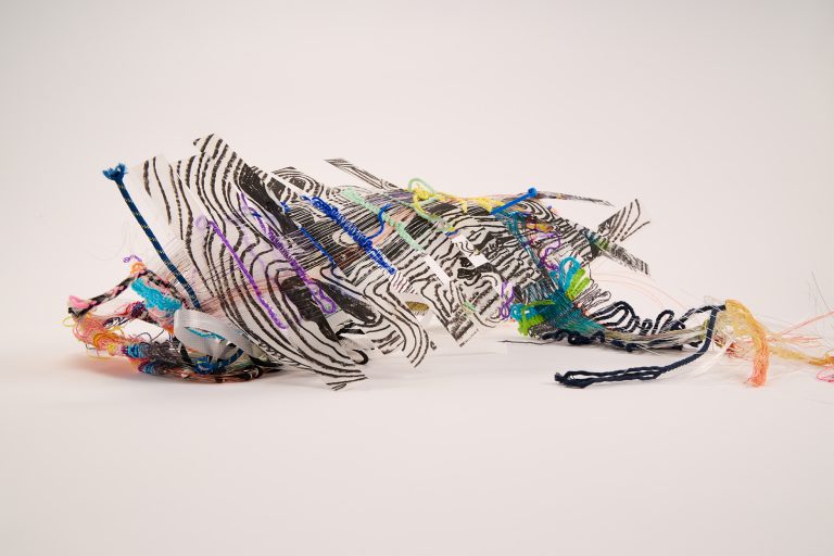 Experimental textile sculpture combining black printed patterns with colourful tangled threads and loose hanging fibres, creating an unstable layered surface suggesting distortion, movement and emotional overload.