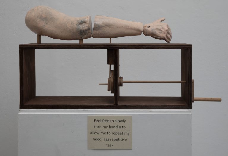 BA Fine Art work by Janet Chase. An automaton arm, bracketed at the elbow. You participate in the narrative, by turning the handle, to repeat my need less repetitive task.
