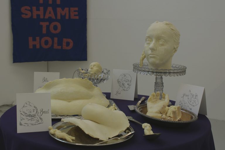 BA Fine Art work by Holly Browning showing a table complete with white chocolate body parts; featuring a head, stomach, breast and hands